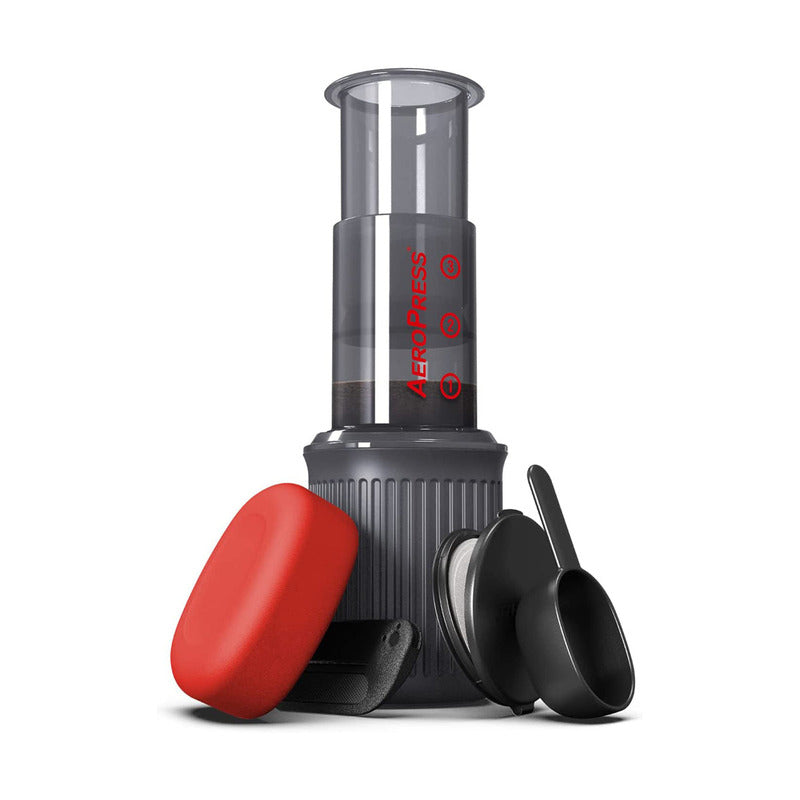 AeroPress Go coffee maker assembled with plunger, chamber, red lid, and included scoop and stirrer.