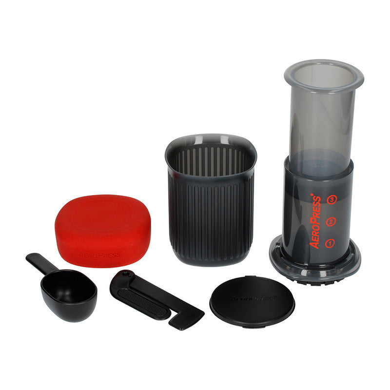 AeroPress Go parts separated, showing chamber, mug, red lid, scoop, stirrer, and filter cap.