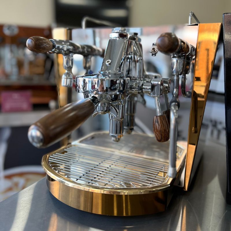 Fracino espresso machine with chrome body, wooden handles, and bronze side panels on a stainless steel counter.
