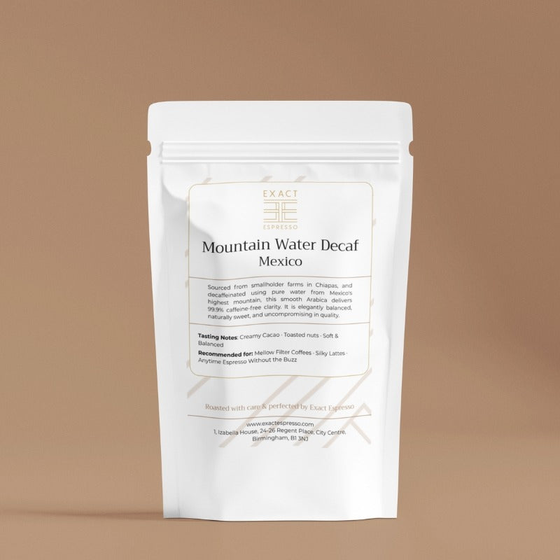 Premium white pouch of Mountain Water Decaf Mexico coffee on a warm tan background, Exact Espresso branding visible.