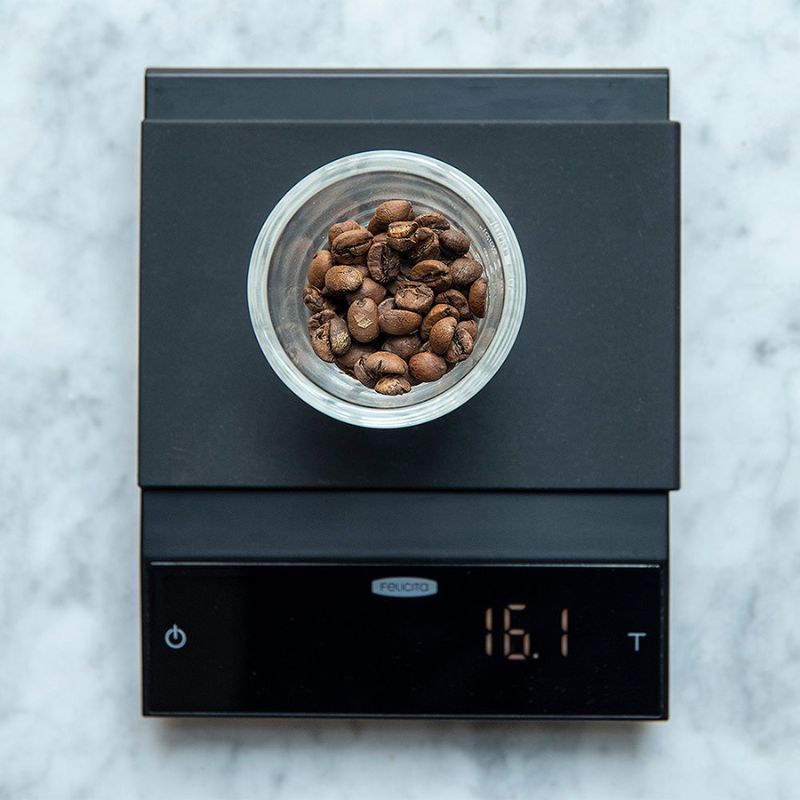 Glass container filled with coffee beans placed on a Felicita incline digital scale displaying 16.1 grams