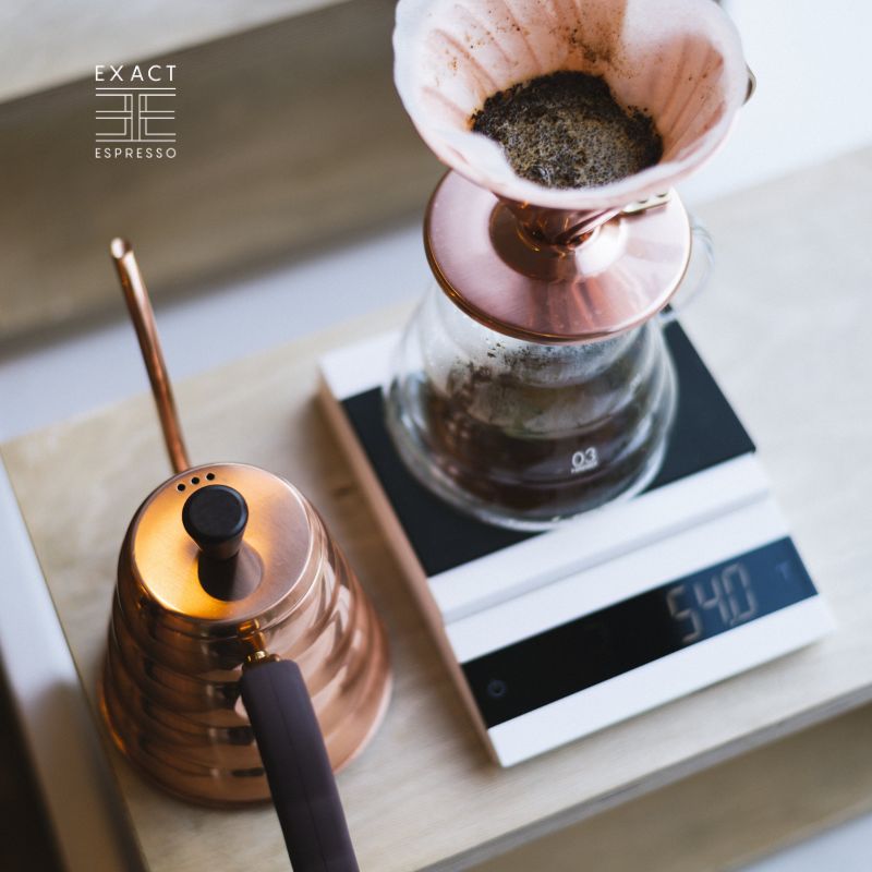 A pour-over coffee setup with a copper kettle and dripper placed on a white felicita coffee digital scale