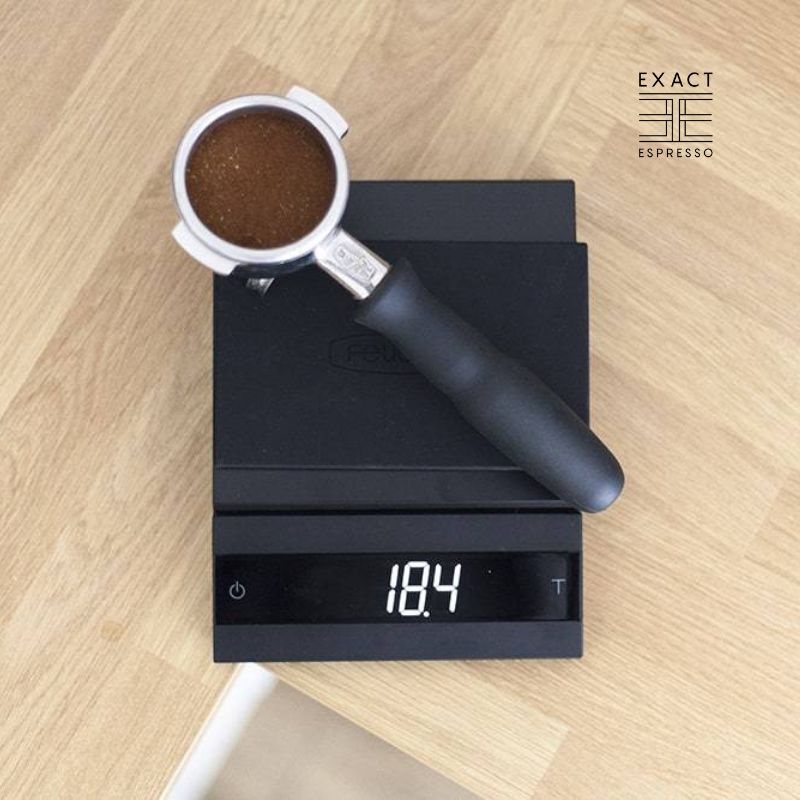A portafilter filled with ground coffee resting on a digital scale displaying 18.4 grams.