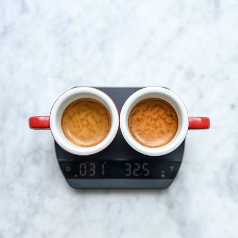 Overhead view of two red espresso cups filled with espresso, sitting on a digital scale that reads 32.5 grams and 0:31 seconds.