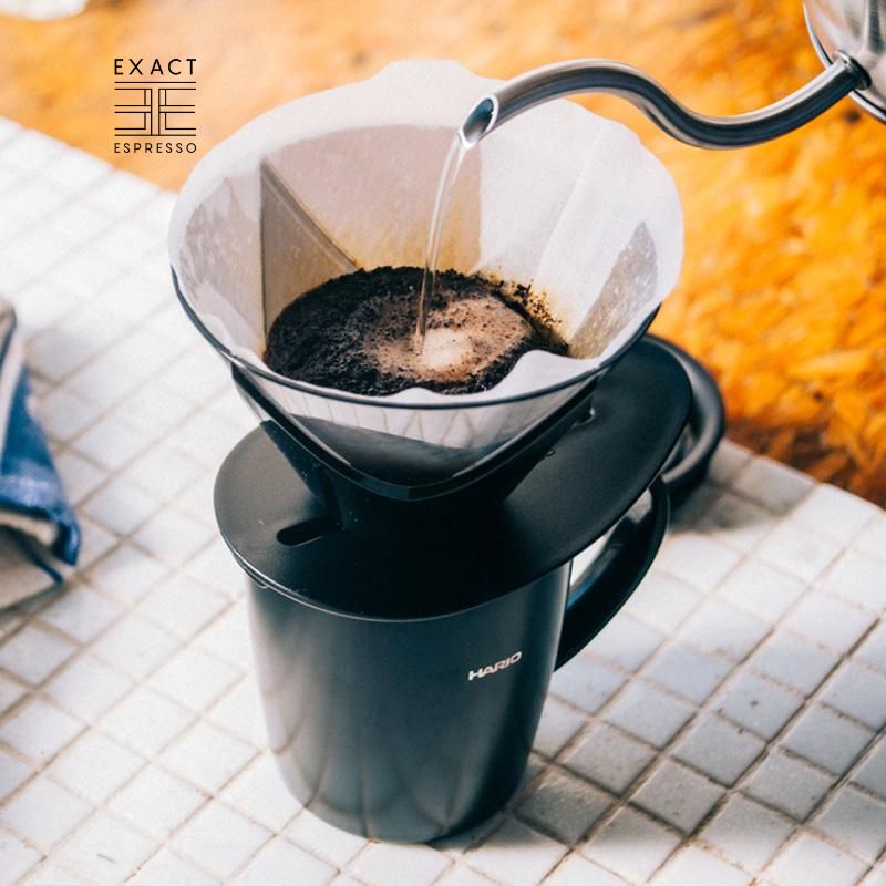 Pour-over Hario V60 with hot water being poured into a paper-filtered dripper atop a black Hario mug.